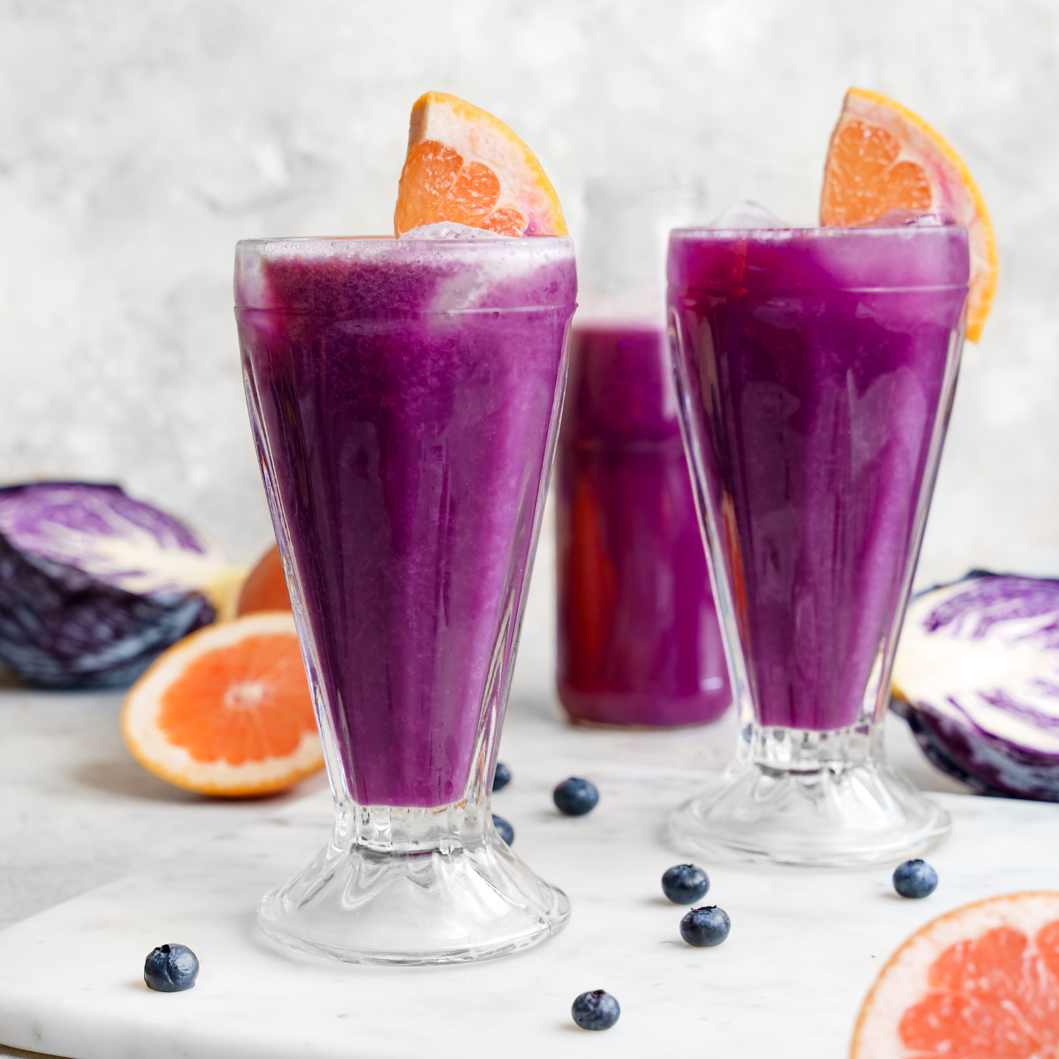 Two glasses of purple juice with a grapefruit wedge on each rim.