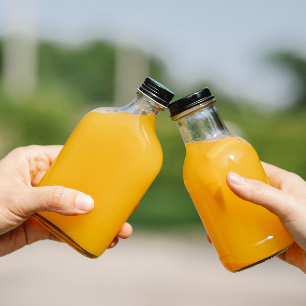 2 people clinking 2 glass bottles of orange juice