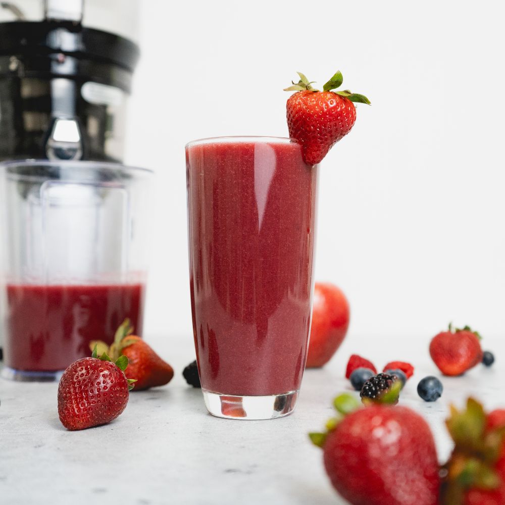 a glass of berry juice with berries surrounding