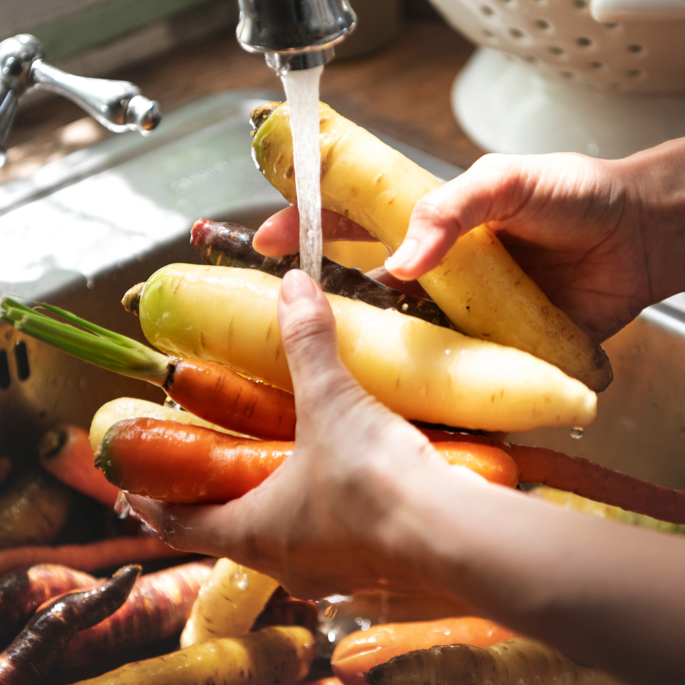 person washing carrots under running water
