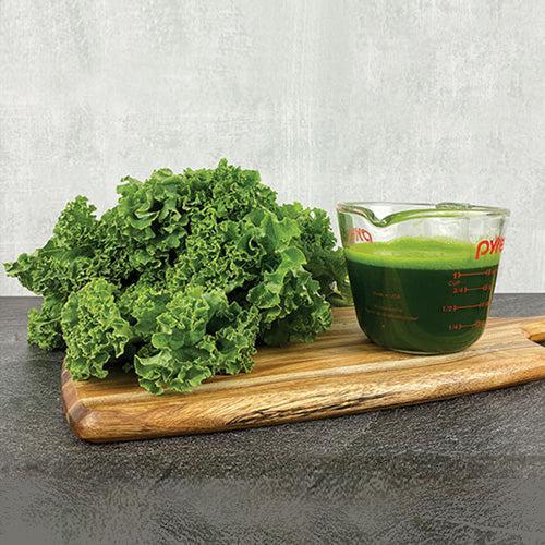 One bunch of kale next to a measuring cup filled with one cup of kale juice.
