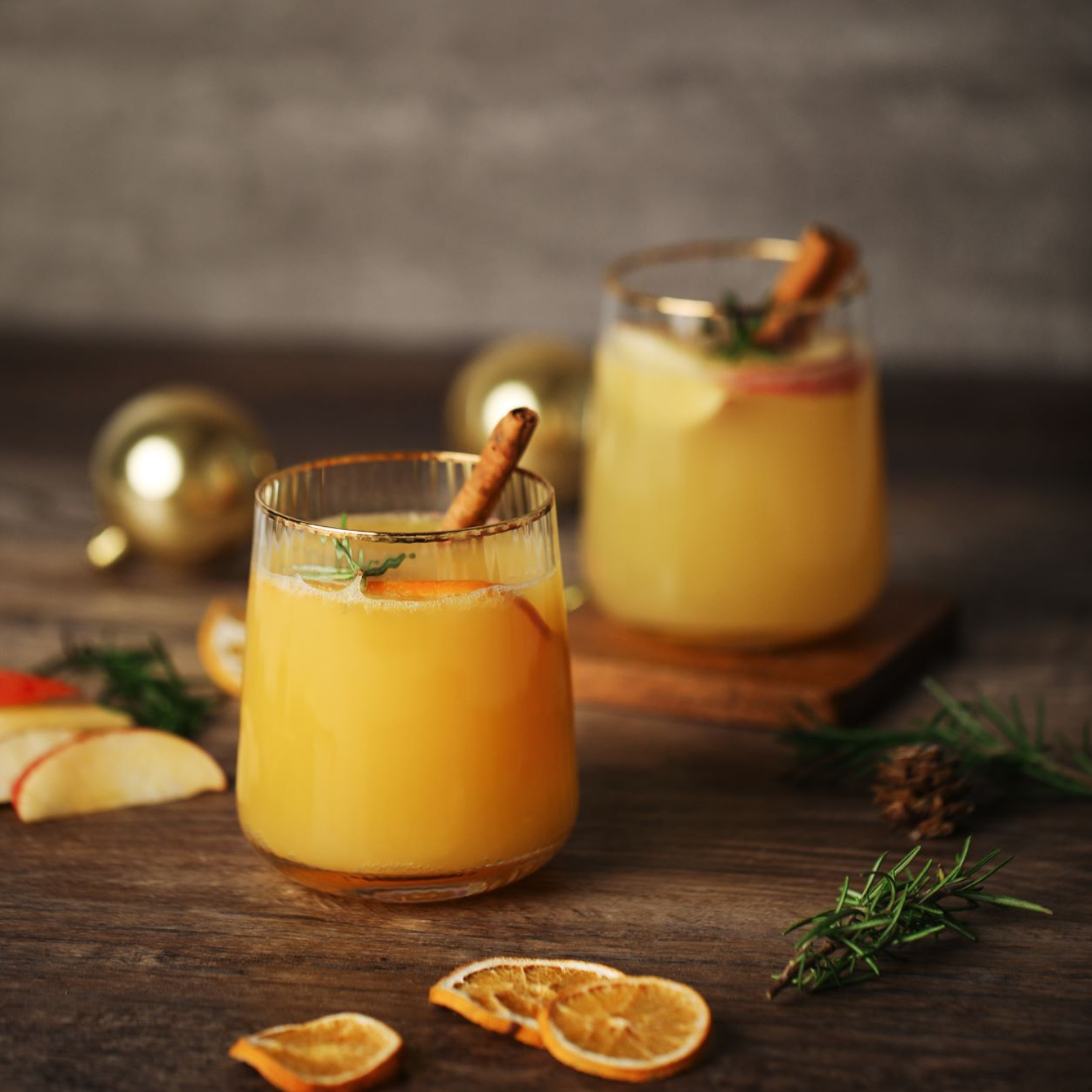 A glass of orange cider in front of a glass of apple cider.