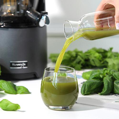 green juice from glass bottle is pouring in cup 
