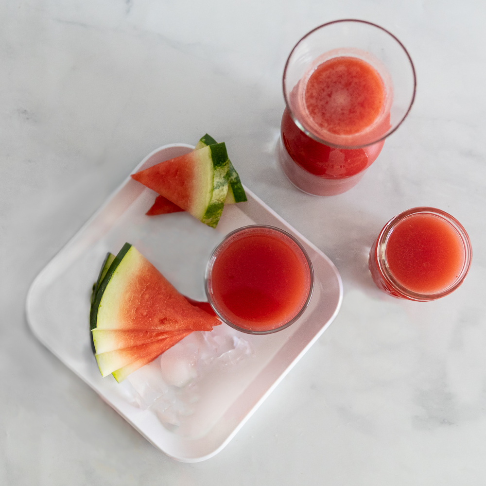 Watermelon slices and watermelon juice and ice on a white tray on marble surface