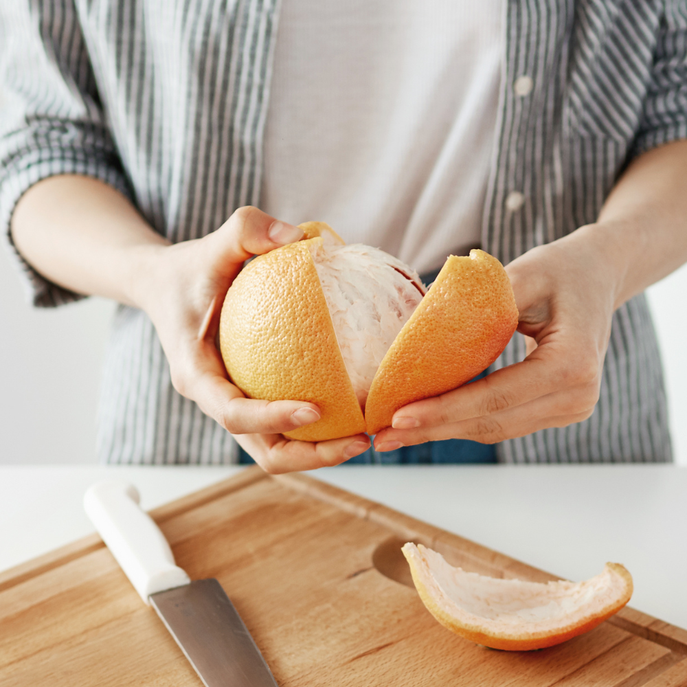 Woman peeling grapefruit over a cutting board and knife