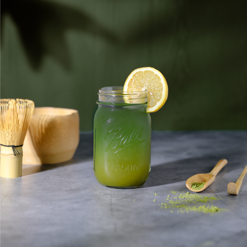 Matcha lemonade drink in a mason jar with matcha powder, matcha bowl, tea whisk, chasaku, & tea spoon