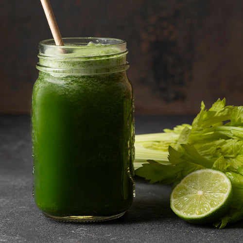 green juice in a jar next to celery and half a lime