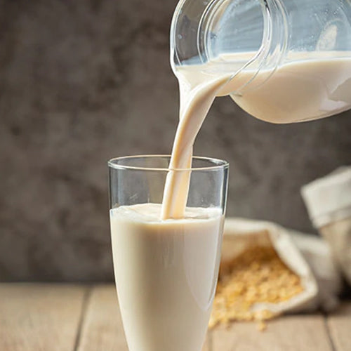 Soy milk poured from a pitcher into a glass