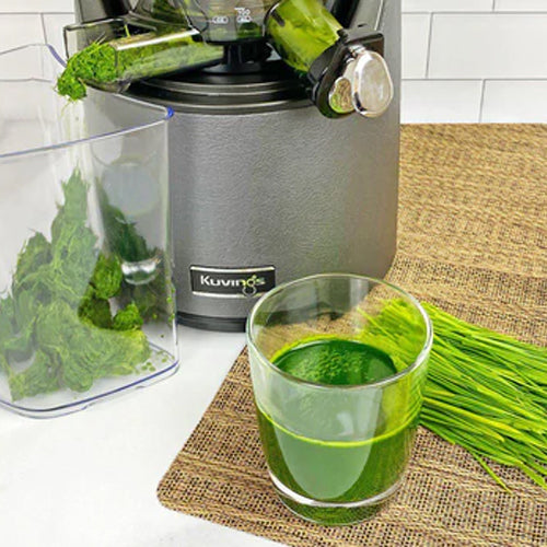 green juice in glass cup with grass, gray juicer