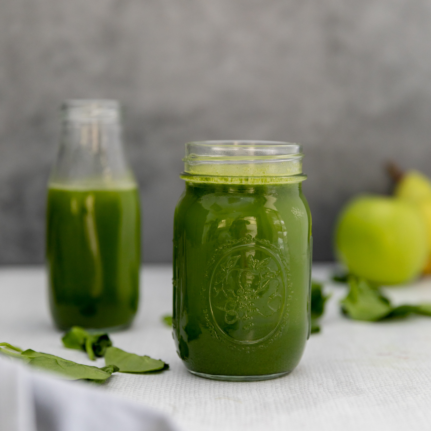 Two glasses of green juice against a gray background.