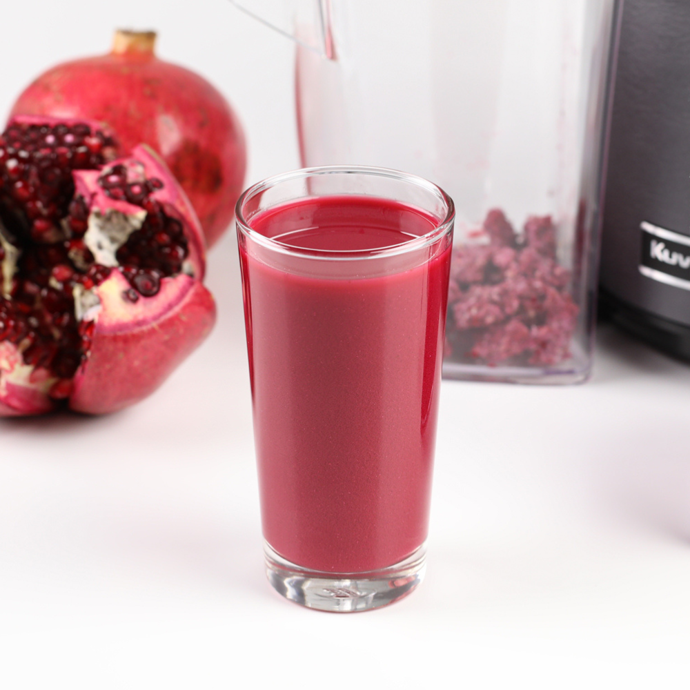A glass of pomegranate juice with pomegranates and pomegranate pulp